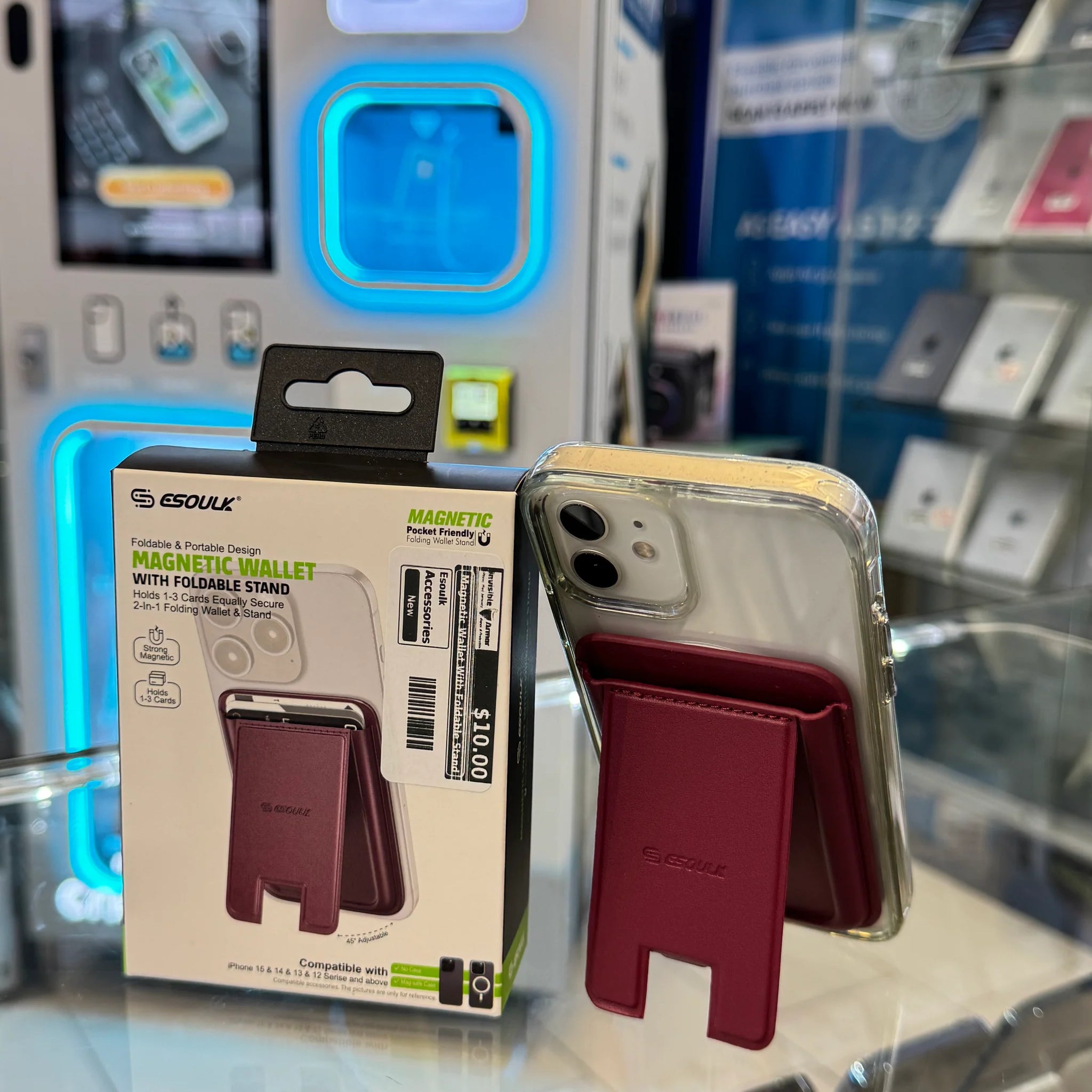 Photograph of an Esoulk Magnetic Wallet with Foldable Stand product box and an iPhone in a clear case with a red-burgundy magnetic wallet attached, displayed on a glass counter in an electronics store with blue glowing display cases and a $10.00 price tag visible