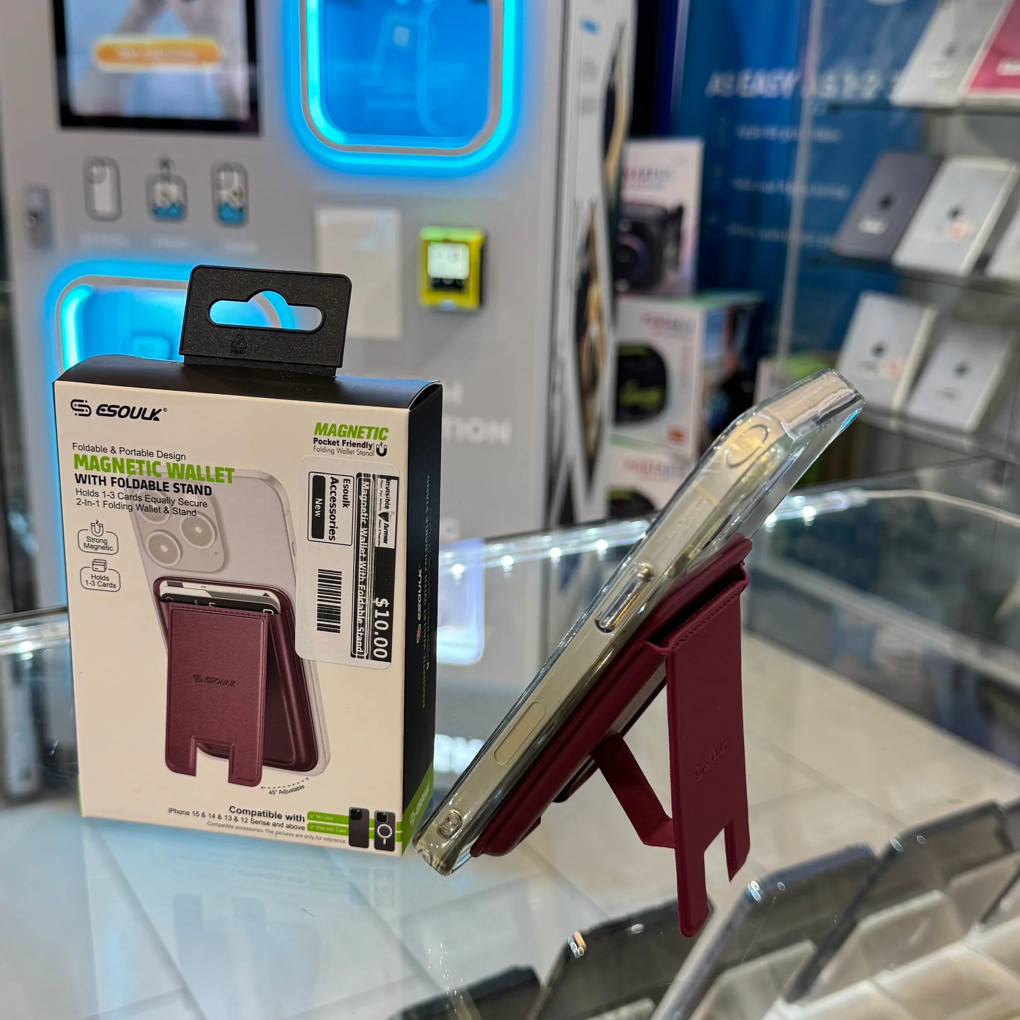 Digital photography featuring an eSoul Magnetic Wallet with a burgundy red foldable stand attached to a clear-cased iPhone 15 on a retail display alongside its packaging and bright blue glowing background elements