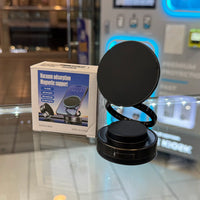 Photograph of a black magnetic phone support with a flexible coiled arm and its white packaging displaying a smartphone, resting on a glass counter in a retail store with blue neon lit displays
