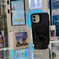 A black carbon fiber iPhone case with an integrated magnetic ring stand and its "Vacuum adsorption Magnetic support" product box sit on a glass counter in a retail electronics store with a blurred blue illuminated phone display in the background