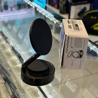 Photograph of a black magnetic phone mount next to its white C-07 instruction box featuring a $20.00 price sticker, displayed on a reflective glass counter with a blurred neon blue light and green logo in the background