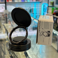 Photograph of a sleek black phone holder with a rotating ring and suction cup base resting on a reflective glass counter in an electronics store, next to a white instruction box detailing its C-07 model features, with a blurry vibrant blue neon light in the background