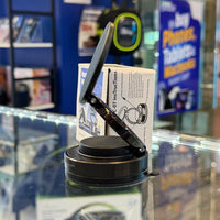Black adjustable phone stand angled on a reflective glass display counter in an electronics store, with a white instruction box and blurry blue signs for phones and tablets behind it