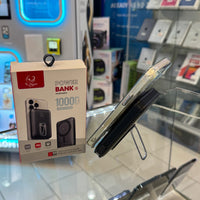Photography of an iPhoenix 10000mAh portable power bank box alongside a silver iPhone in a clear case with an attached black magnetic power bank showing 52% charge, all displayed on a glass counter in an electronics store featuring blurred colorful phone cases and a glowing blue square display in the background